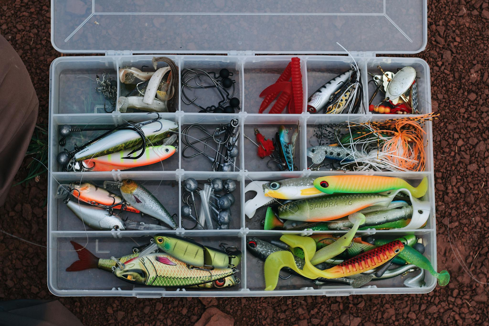 A top view of a tackle box filled with various colorful fishing lures and equipment.