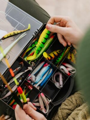 Bright fishing lures and equipment in an organized tackle box being handled.