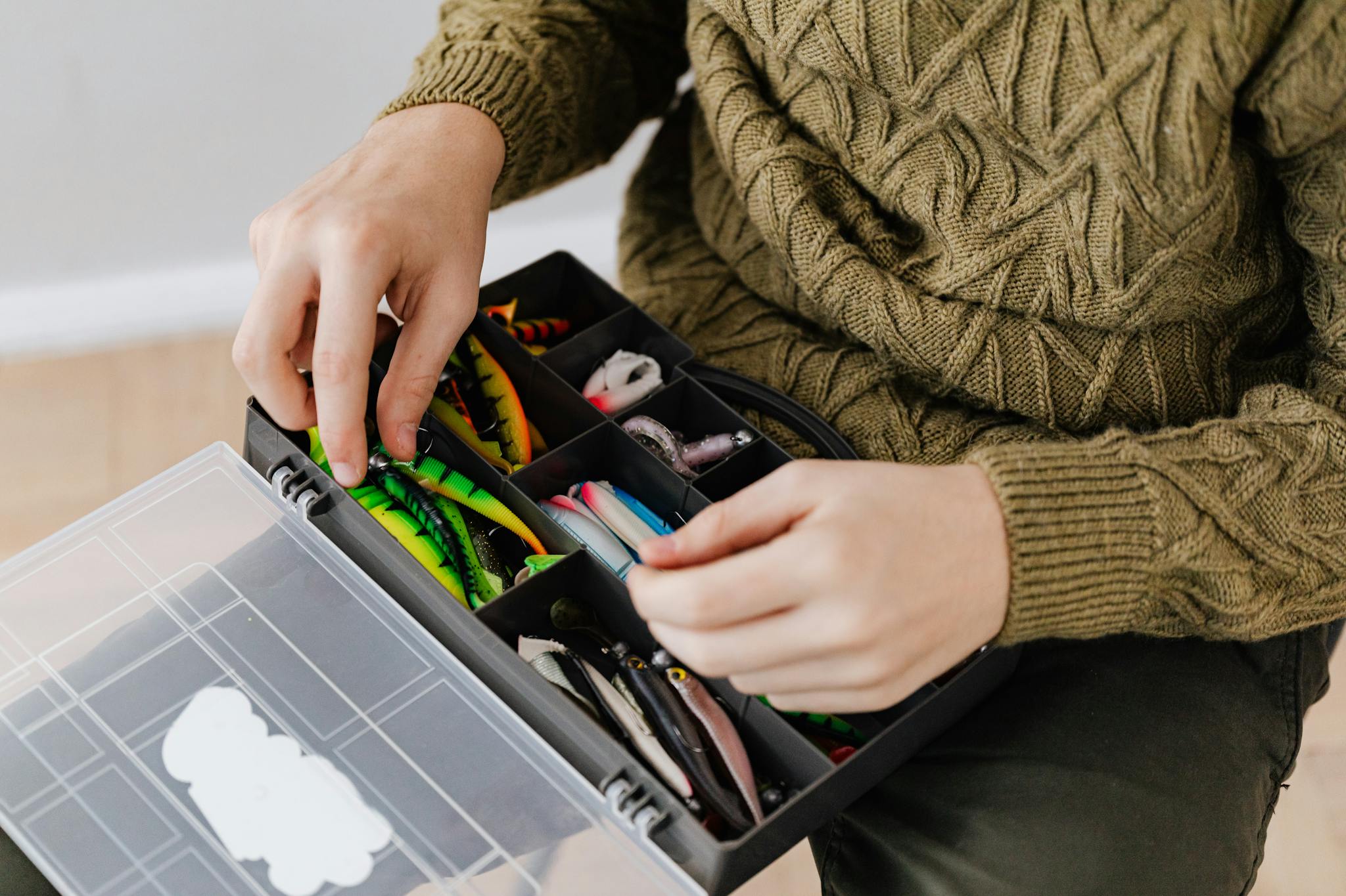 Close-up of hands arranging fishing lures in a tackle box, indoors.