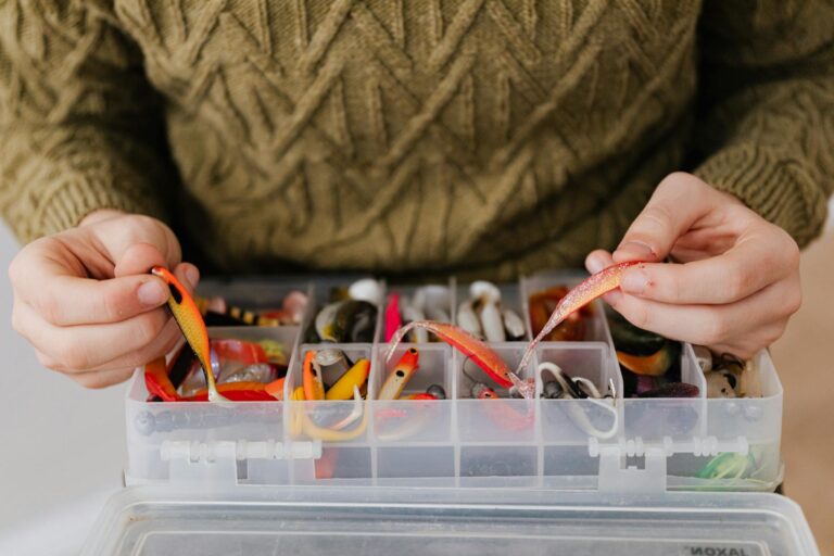 Close-up of hands organizing colorful fishing lures in a tackle box, perfect for anglers.